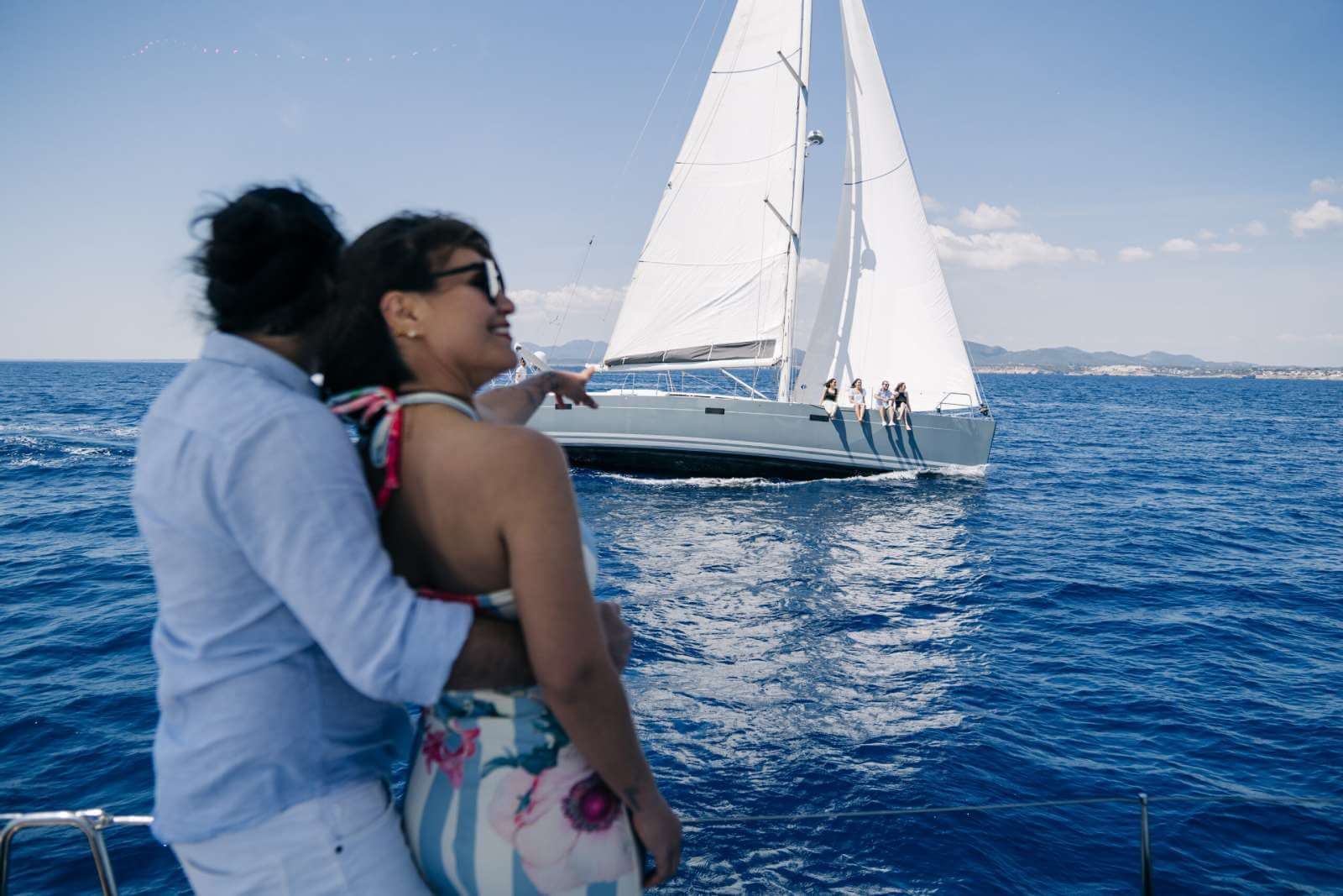 Pareja a bordo con el velero Meltemi navegando al fondo